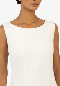 Abito bianco senza maniche con scollatura rotonda, texture morbida e silhouette aderente. Dettagli di cucitura sottili sono visibili sul torso.