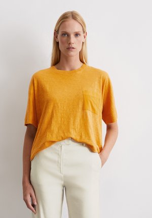 Żółta krótki rękaw t-shirt wykonany z lekkiego materiału, z kieszonką na klatce piersiowej i luźnym krojem, zestawiony z jasnymi spodniami.