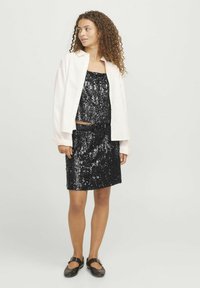 Top e gonna coordinata nera in paillettes, sovrapposti a una camicia bianca con bottoni. L'outfit presenta un design aderente e una texture lucida. Scarpe nere senza tacco.