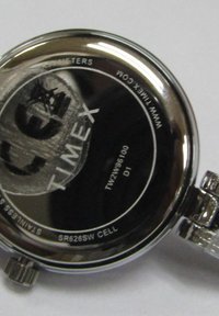 Montre en acier inoxydable argenté avec un boîtier rond et une finition texturée. Comprend une couronne et des détails gravés à l'arrière, y compris "TIMEX."