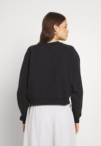 Felpa nera con colletto a girocollo, maniche raglan e orlo a costine. Tessuto morbido, design aderente, texture liscia e dettagli minimi.