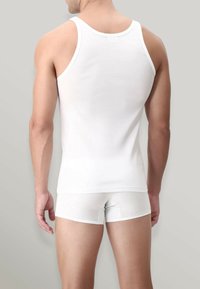 Top in cotone bianco, dalla vestibilità aderente, con spalline larghe e schiena senza cuciture. Indossato con boxer bianchi coordinati.