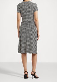 Czarna i biała sukienka w deseń houndstooth z krótkimi rękawami, dopasowaną talią i spódnicą do kolan, zestawiona z czarnymi sandałami na wysokim obcasie.