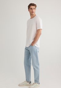 Light pink short-sleeve t-shirt, relaxed fit, paired with light blue straight-leg jeans. Footwear features white base with green accents.