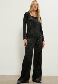 Zwart, fluwelen loungewear set met lange mouwen en vierkante halslijn. Beschikt over een relaxte pasvorm en een glanzend zilveren stippenpatroon. Brede pijpen.