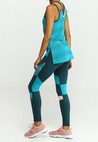 Turkos linne med meshpaneler, kombinerat med teal- och blåmönstrade leggings. Rosa träningsskor fulländar outfiten.