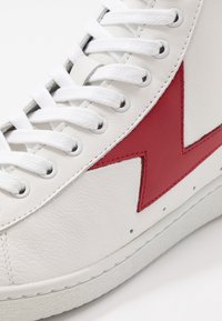 Baskets en cuir blanc avec lacets blancs, motif éclair en cuir rouge sur le côté et semelle en caoutchouc blanche.