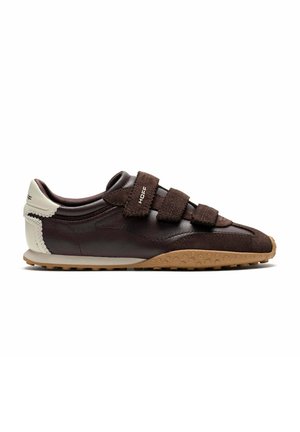 Zapatilla de perfil bajo color marrón oscuro con tres tiras de velcro, talón beige y suela texturizada marrón claro.