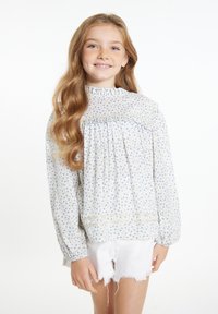 Lyseblå blomstermønstret bluse med lange ærmer, samling i halsudskæringen og livstykket, parret med hvide slidte shorts. Blødt stof.