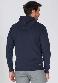 Haut à capuche bleu marine en coton doux, avec un cordon de serrage, des poignets côtelés et une taille ajustée. Design uni sans motifs.