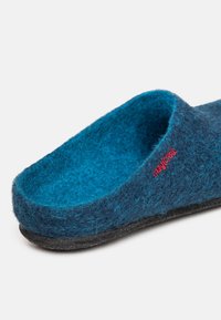 Pantofola in feltro di lana blu scuro con superficie testurizzata; presenta un logo rosso e una suola in gomma nera per una maggiore durata.