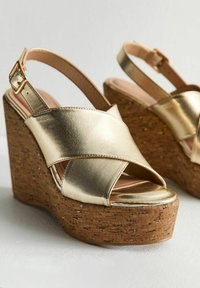 Sandales à talon compensé en métal doré avec plateforme en liège. Bretelles croisées à l'avant, bride de cheville réglable et texture en cuir lisse.