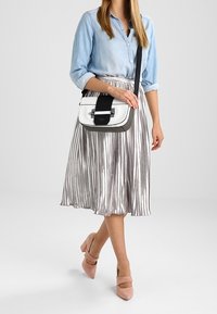 Bolso de hombro en blanco y gris, con una correa negra y herrajes en plateado. Combinado con una camisa azul claro y una falda a rayas metálicas.