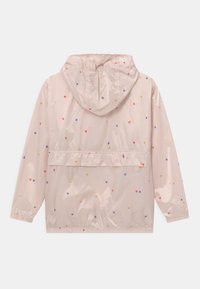 Chaqueta de lluvia con capucha de color rosa claro, con pequeños lunares multicolores y mangas elásticas, mostrada desde la parte posterior sobre un fondo blanco.