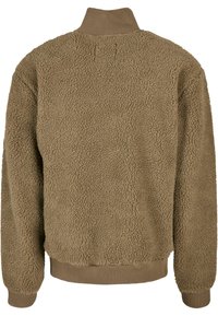 Bruine fleece jas met een gestructureerd oppervlak, hoge kraag en geribbelde manchetten en zoom. Achteraanzicht toont zacht, pluche materiaal en een oversized vorm.