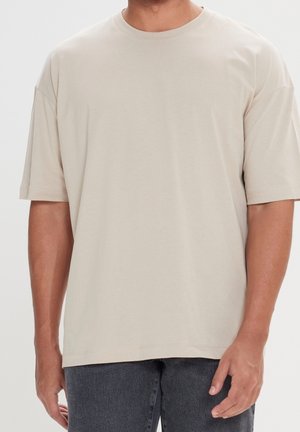 Beige t-shirt lavet af blødt stof, med rund hals og korte ærmer. Løs pasform med lige bundkant, glat tekstur.