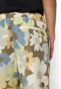 Pantaloni corti floreali con un motivo di grandi fiori multicolori in sfumature di blu, verde e beige. Include una cintura elastica e un dettaglio del logo.