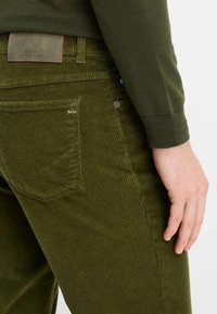 Olijfgroene corduroy broek met een getextureerd geribd patroon, voorzien van achterzakken en een lederen merklabel bij de taille.
