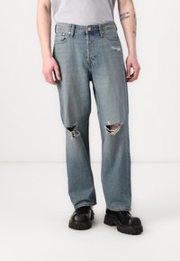 Lyseblå ripped jeans med slitte områder på knærne, rett benpassform, og metallknapplukking. Brukt med svarte sko med tykk såle.