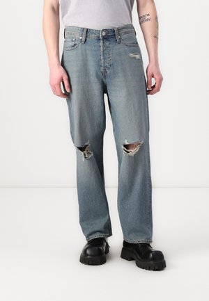 Lyseblå ripped jeans med slitte områder på knærne, rett benpassform, og metallknapplukking. Brukt med svarte sko med tykk såle.