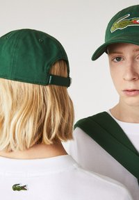 Gorra de béisbol verde de algodón con un logo en la parte frontal, correa ajustable y tejido texturizado. Sudadera blanca con un pequeño logo en la parte posterior.