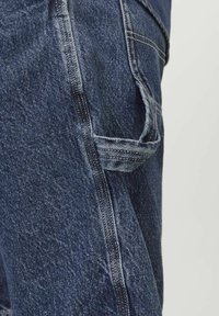 Pantalones cargo de mezclilla en azul oscuro con un acabado texturizado. Presenta múltiples detalles de bolsillos y costuras en contraste a lo largo de las costuras.