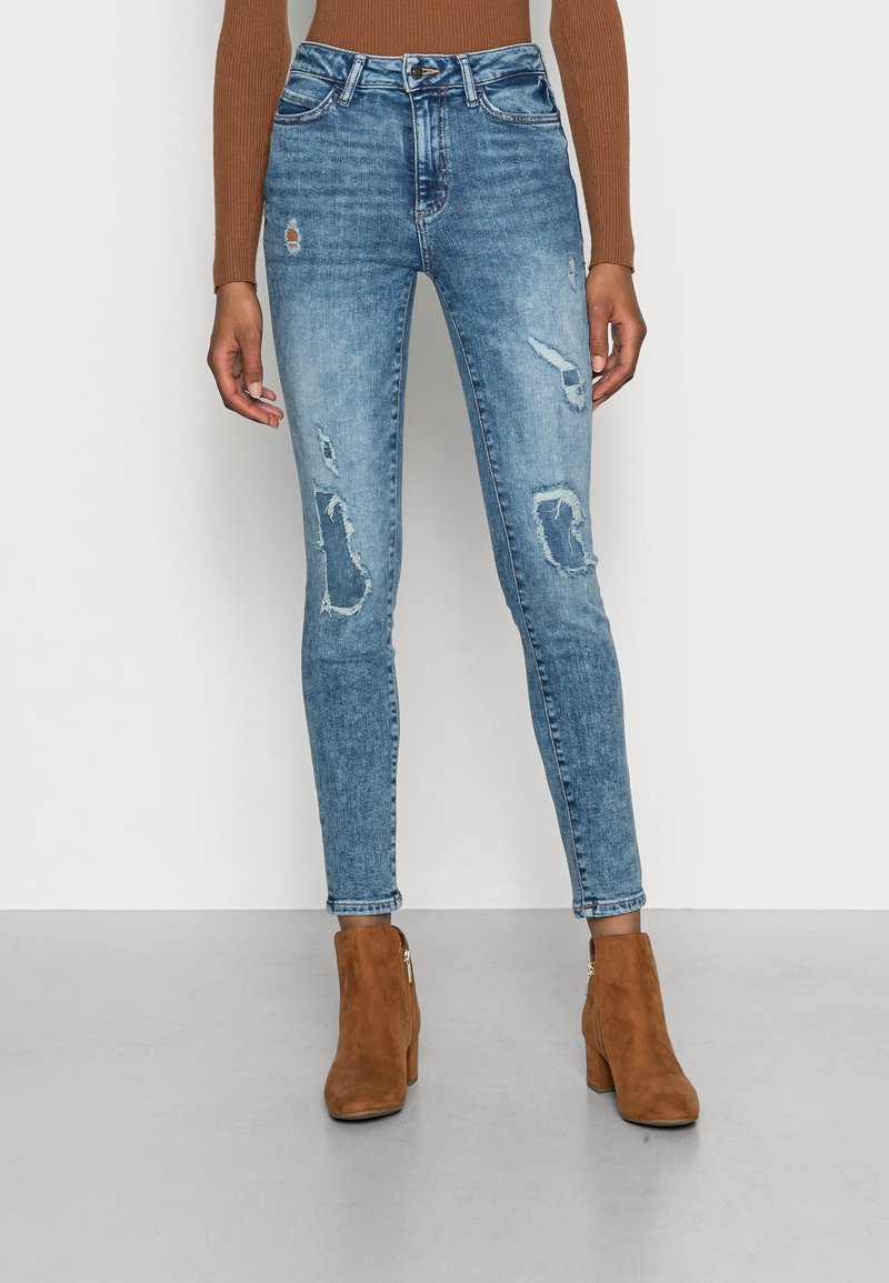 Jean bleu clair slim délavé associé à des bottines en daim marron et un haut à manches longues couleur rouille.