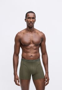 Boxer da uomo verde oliva con una fascia in vita nera con il logo "BJÖRN BORG", materiale in cotone, design aderente e una texture liscia.