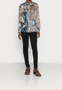 Personne portant une chemise à manches longues à boutons avec des motifs mixtes d'animaux et floraux, un pantalon noir slim et des sandales à talons noires à lanières.