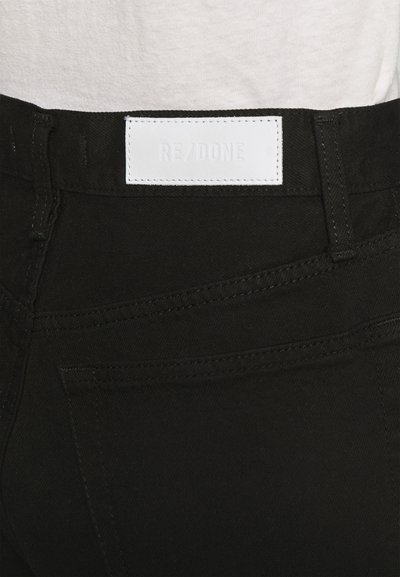 Black denim jeans with a smooth texture and contrasting stitching. Features a white leather patch labeled "RE/DONE" on the back waistband.