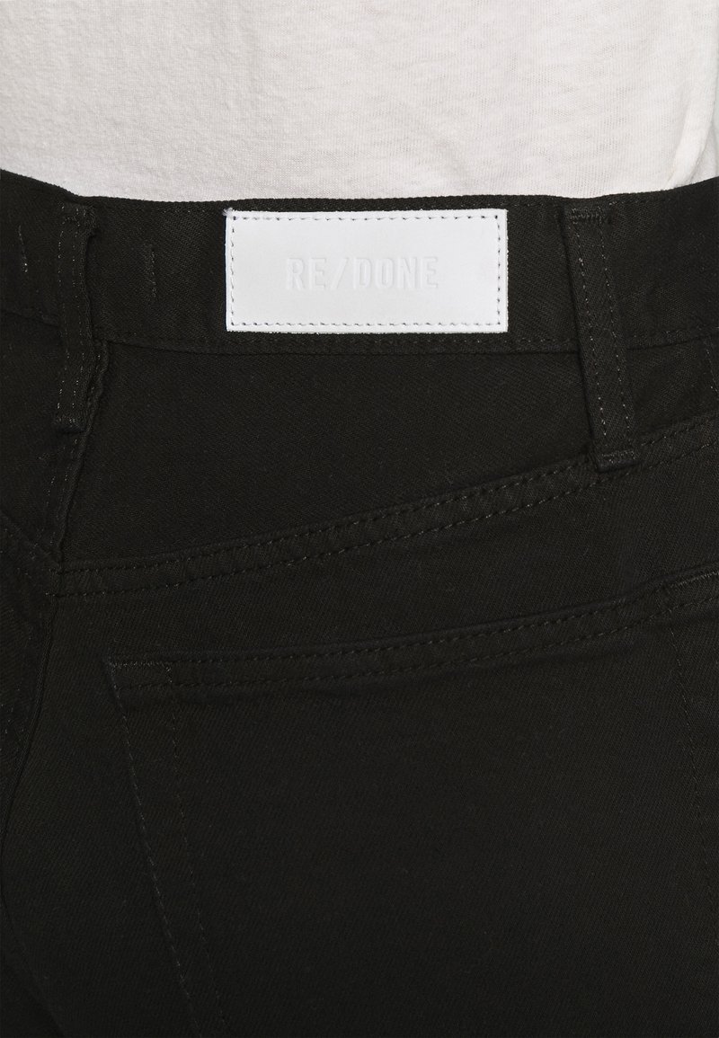 Schwarze Denim-Jeans mit glatter Textur und kontrastierenden Nähten. Verfügt über ein weißes Lederetikett mit der Aufschrift "RE/DONE" am hinteren Bund.