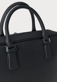 Fekete bőrből készült aktatáska texturált, dupla fogantyúkkal és ezüstszínű fém díszítéssel, az elülső részén enyhén dombornyomott „BOSS” logóval.