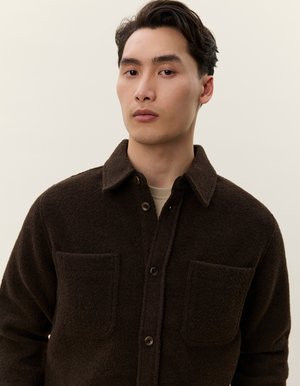 Giacca camicia in lana marrone con chiusura a bottoni, due tasche sul petto e un tessuto strutturato. Presenta un colletto classico e bottoni scuri.