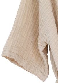 Šviesiai smėlio spalvos medvilninė tekstilė su tekstūruota, siuvinėta paviršiaus danga ir banguotomis kraštinėmis. Audinys minkštai krenta.