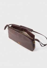 Kožená kabelka v tmavě hnědé barvě s hladkým povrchem, zipovým uzávěrem a nastavitelným popruhem. Disponuje zlatými detaily pro přidanou eleganci.