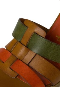Leather sandal featuring woven straps in orange, green, and brown, with a smooth texture and contrasting inner lining in red.