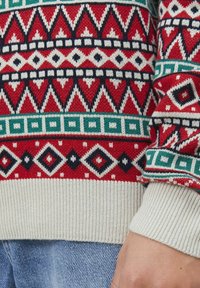 Gebreide trui met een rood, marineblauwe en groene geometrische print met diamant- en driehoekmotieven. Ribbelboord in crème aan de onderkant en mouwen.