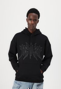 Black hoodie with a front pocket, featuring a shiny studded graphic design. Loose fit, made of soft fabric, with drawstrings on the hood.