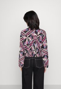 Blusa de manga larga con un patrón geométrico multicolor en rosa, negro y azul; acompañada de unos vaqueros de pierna ancha oscuros con costuras blancas.