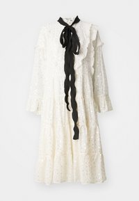 Rochie albă cu guler și manșete volănate, având un săculeț cu panglică neagră și un material texturat cu paiete. Design stratificat cu o siluetă fluidă.