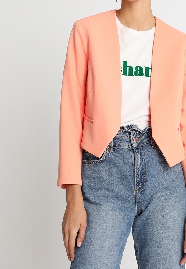 Femme portant un blazer court pêche sur un t-shirt blanc imprimé graphique, rentré dans un jean bleu taille haute avec une taille paperbag.
