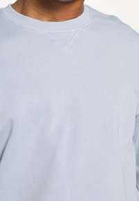 Světle modrý sweatshirt s kulatým výstřihem vyrobený z měkké bavlny, s žebrovaným límcem a jemným V-švem v oblasti krku.