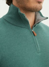 Pullover zippé vert avec un col haut, texture en maille et doublure intérieure grise. Présente un accent en cuir sur la tirette.