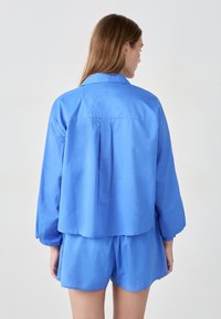 Niebieska, lekka koszula z krótkim rękawem i kołnierzykiem, z zakładką z tyłu i luźnym krojem. W zestawie z pasującymi niebieskimi szortami.