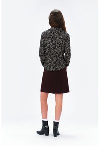 Blouse noire à motifs avec de petites formes blanches et rouges, accompagnée d'une jupe bordeaux. Le modèle porte des bottines noires à finition brillante.