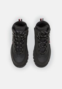 Czarne sneakersy w wysokim kroju z teksturowanej tkaniny, trwałą podeszwą i kontrastującymi białymi oraz czarnymi sznurowadłami. Posiadają metkę z logo i czerwony akcent.