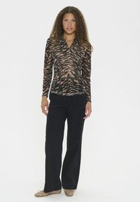 Langärmliges Oberteil aus transparenter Stoff mit einem Tigerprint in Schwarz und Braun, kombiniert mit schwarzen weiten Hosen und mit Nieten besetzten beigen Ballerinas.
