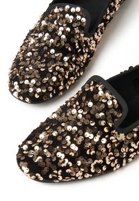 Zapatos negros tipo slip-on cubiertos de lentejuelas de bronce, con una textura suave y ribete elástico en la abertura para un ajuste ceñido.