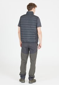 Graue isolierte Weste mit horizontalen Nähten, kombiniert mit grauen Hosen mit dunklen Akzenten und strapazierfähigem Schuhwerk. Verstellbarer Kragen.