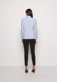 Camicia manica lunga azzurro chiaro con colletto abbottonato, vestibilità sartoriale e dettaglio dello sprone posteriore, abbinata a pantaloni neri aderenti e tacchi.